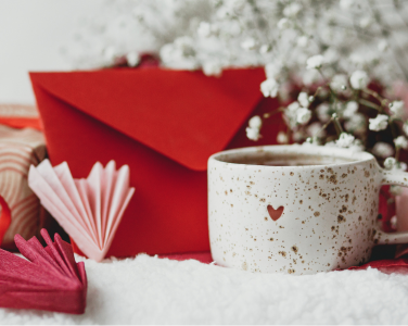 A mug with a heart surrounded by a red envelope and flowers.