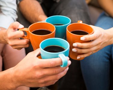Hands holding orange and blue coffee mugs in a toasting gesture.