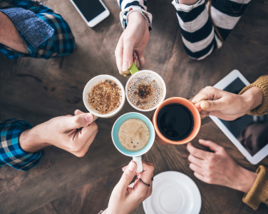 Four hands holding coffee mugs in a toast