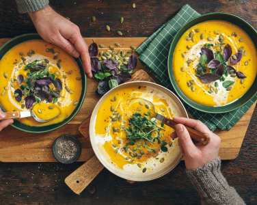 Top-down view of three bowls of soup on a wooden table.