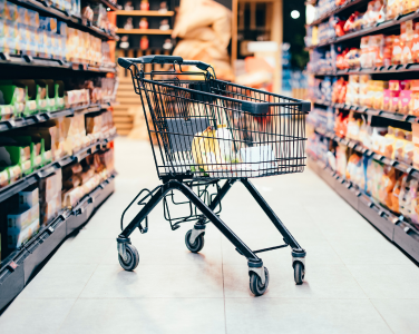 Empty shopping cart in a grocery store aisle surrounded by shelves of products.