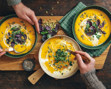 Bowls of soup garnished with herbs on a wooden board.