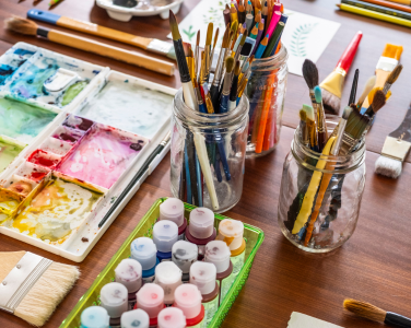 Jars of brushes and acrylic paints on a wooden table.