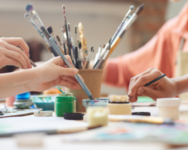 Hands holding paint brushes and painting supplies.