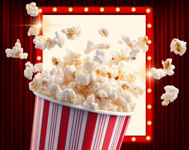 Popcorn bursting from a striped container in front of a lit marquee sign.