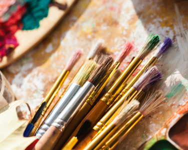 Assorted paintbrushes on a paint-covered surface.