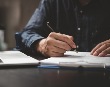 Person writing with a pen while sitting at a desk.