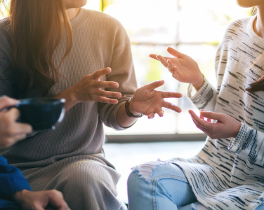 Three people sitting and chatting with communicative hand gestures.