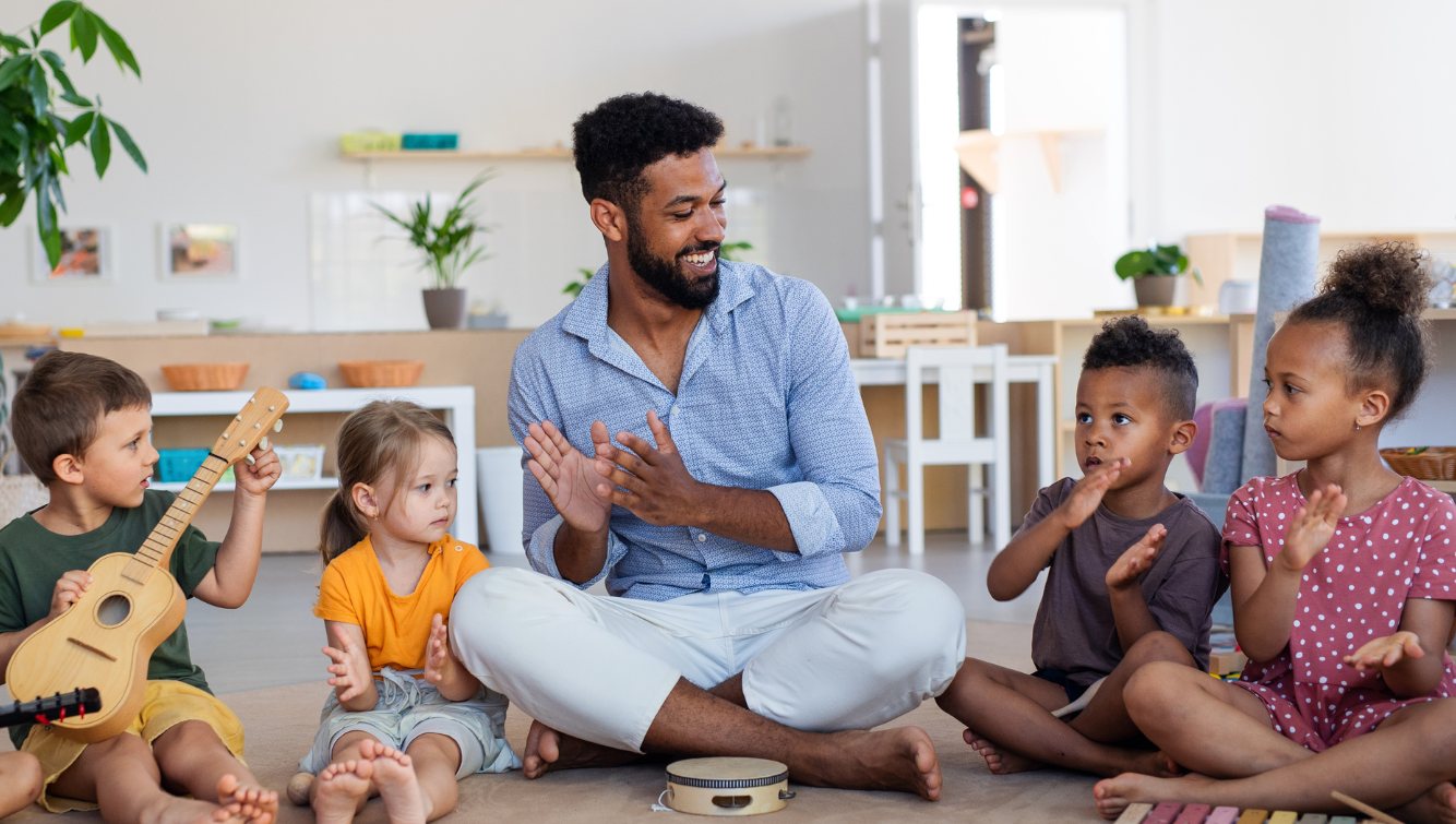 A teacher and children sitting on the floor, clapping and playing instruments.