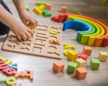 Child assembling an alphabet puzzle with colorful blocks and rainbow arches.