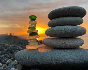 Stacked stones and sea glass with a sunset on a rocky beach.