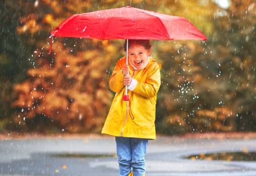 young girl standing in the rain under a red umbrella