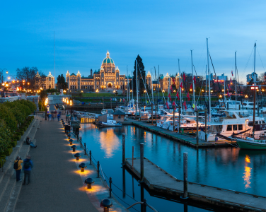Downtown Victoria marina at dusk with illuminated parliament buildings.