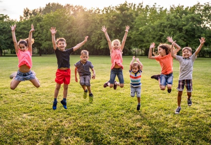 Children jumping happily together on a grassy field outdoors.