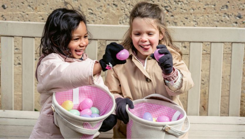 Two children enjoy an Easter egg hunt outdoors, holding colourful eggs and baskets.