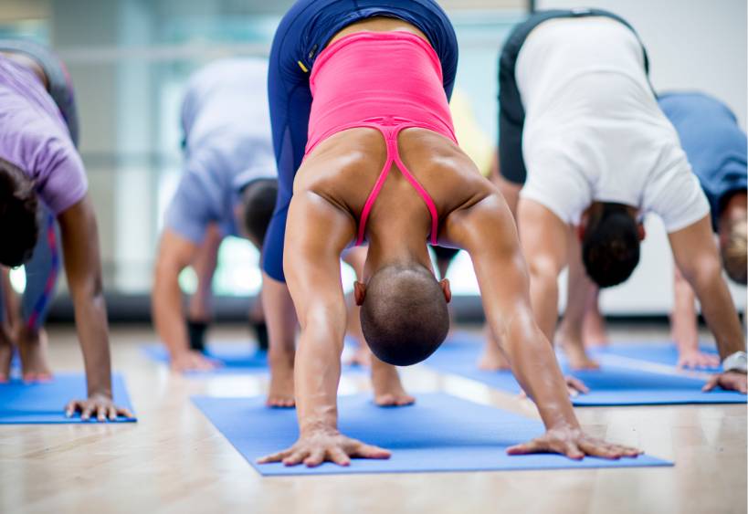 A group of men and women doing yoga together on exercise mats in a fitness centre.