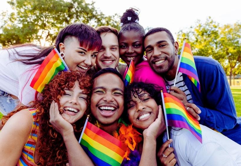  Cheerful, multi ethnic friends embracing and laughing together while proudly holding small rainbow flags