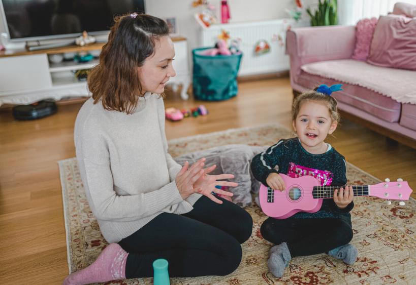 Babysitter and young child who is playing ukulele