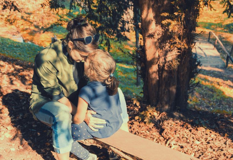 Mother and her small daughter sitting face to face on a bench in nature