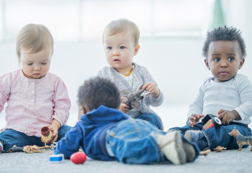 Babies of 12-17 months sitting on a carpet inside playing together with blocks and animal toys
