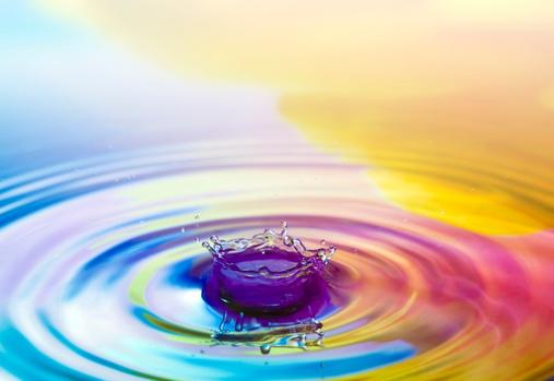A waterdrop falling down into the rippled colored water.