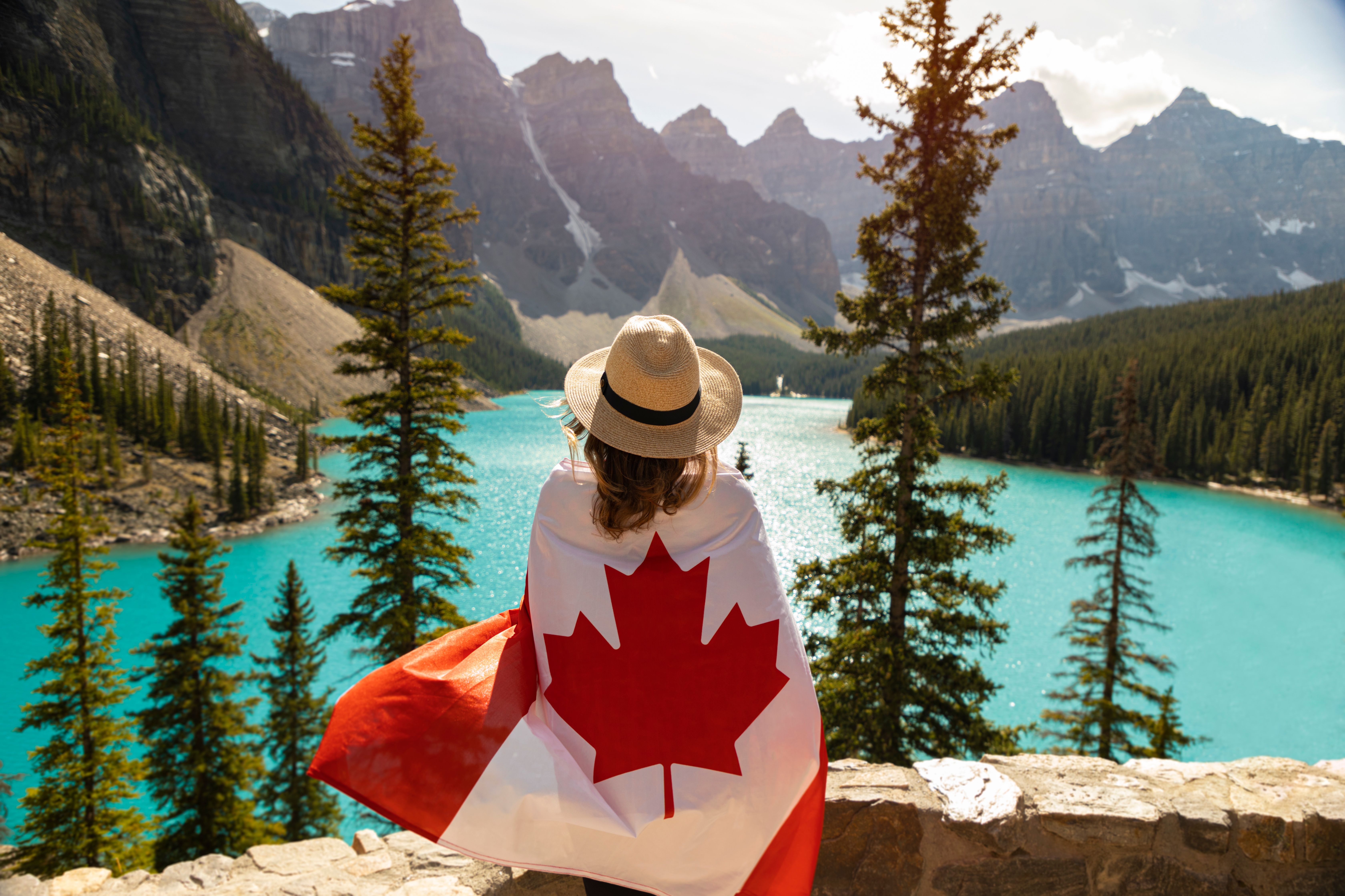 woman with Canadian flag wrapped around her looking at a lake in between mountains
