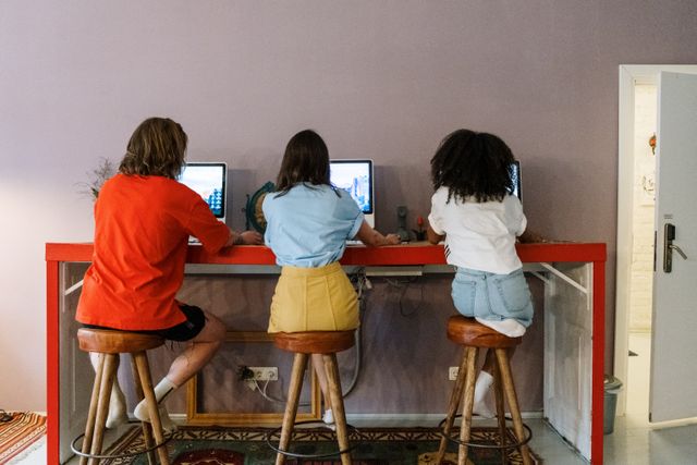 Three people working on computers in a modern indoor setting with wooden stools.