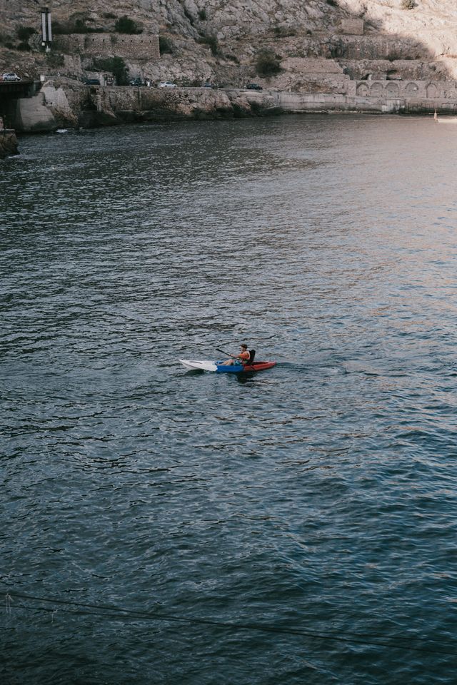 A kayaker paddles through serene coastal waters surrounded by rocky cliffs, captured in a dynamic vertical shot.