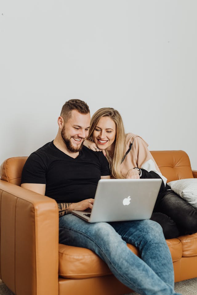 Happy couple enjoying time on couch using laptop together indoors.
