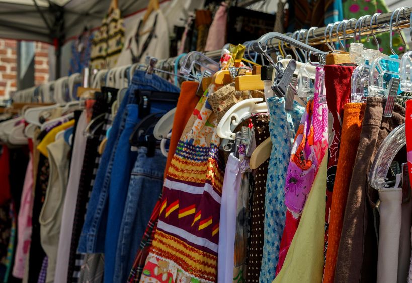 Clothing rack filled with colourful garments on hangers, set up under a tent at a clothing swap event.