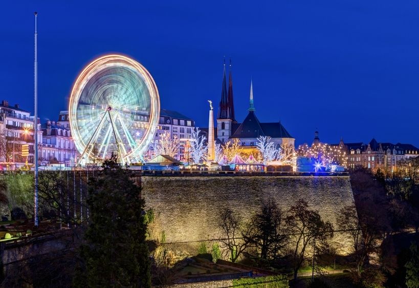 A brightly lit Ferris wheel overlooks a festive Christmas market in the heart of a historic city.