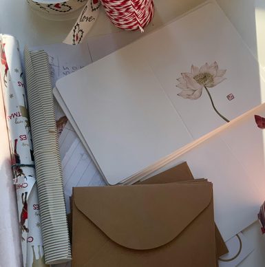 a table covered with various card-making supplies, like ribbon, cardstock, brown envelopes, and rolls of patterned paper