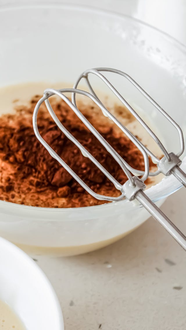 Close-up of an eggbeater and cocoa powder in a bowl, perfect for baking themes.
