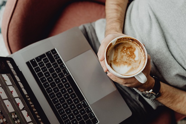 person holding a cup of coffee while looking at online meet on a laptop