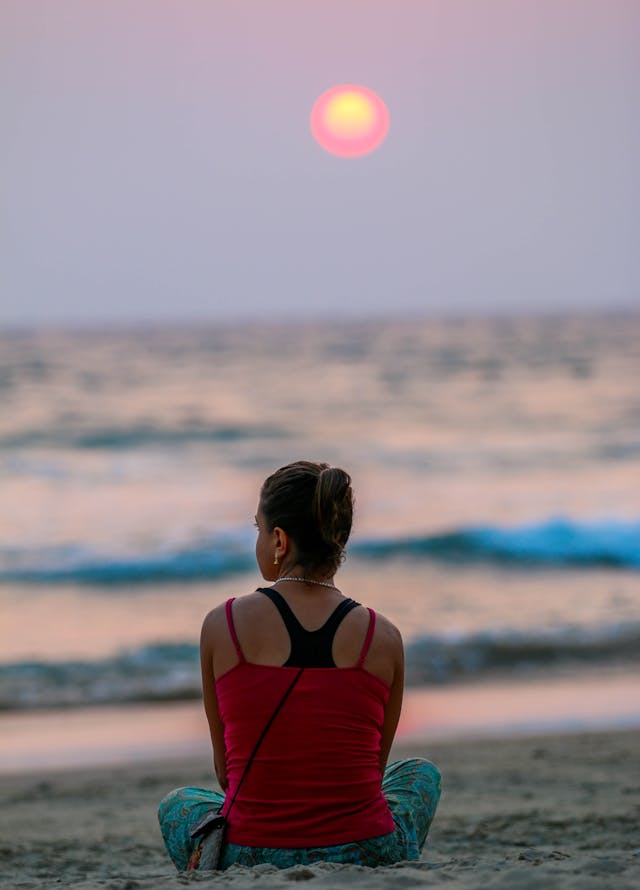 A Woman in Red Tank Top Sitting on Beach during Sunset