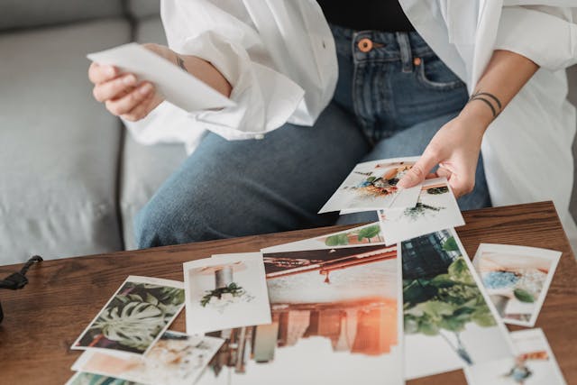 Crop woman at table with various photos at home