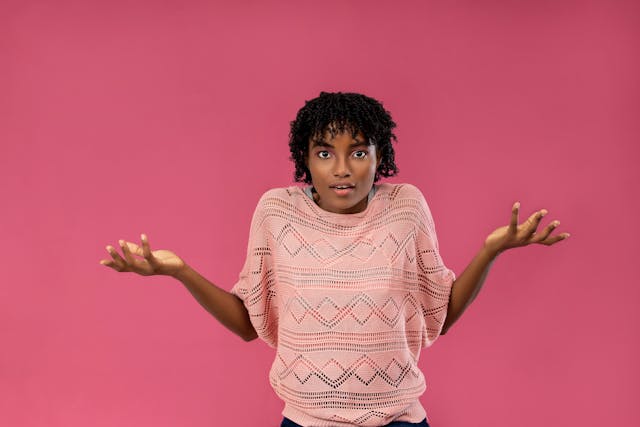 Puzzled Woman Shrugging in Pink Studio Background