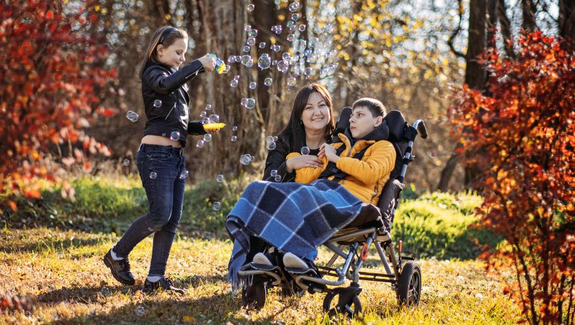 woman child in wheelchair and child making bubbles in forest