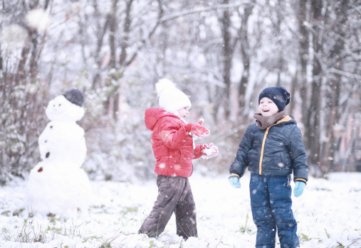 a 3 year old boy and girl in snow gear playing in the snow and building a snow man