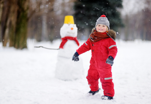 2 year old child in red snowsuit building a snowman