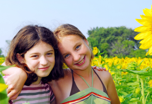 two preteen girls standing arm in arm in a sunflower field