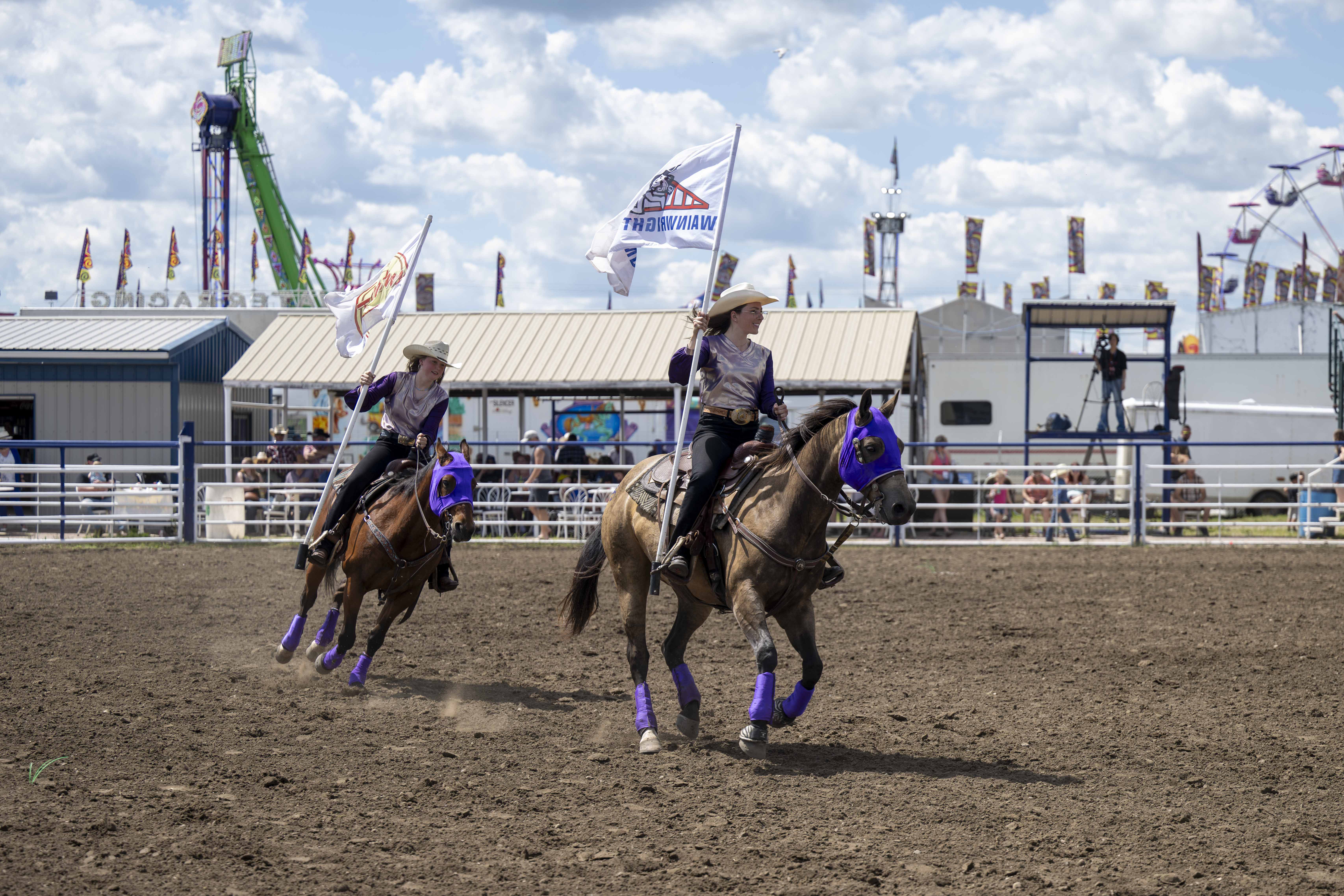 Two cowgirls on horses with flags.
