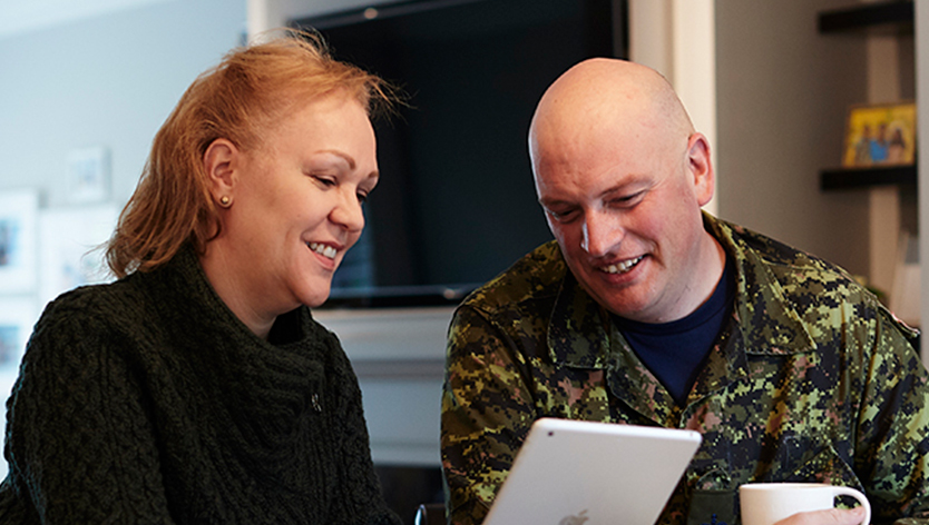 A military couple, smiling, having coffee while looking at a tablet