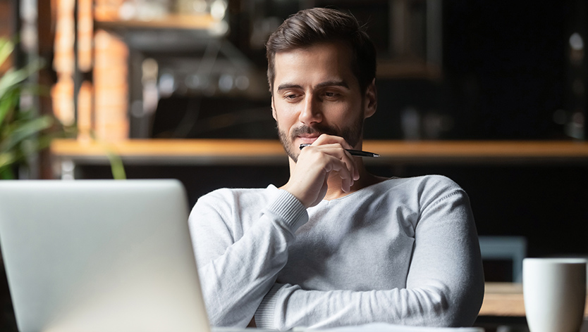 man holding pen looking at laptop