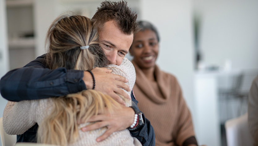 A man is hugging a female during a group therapy session