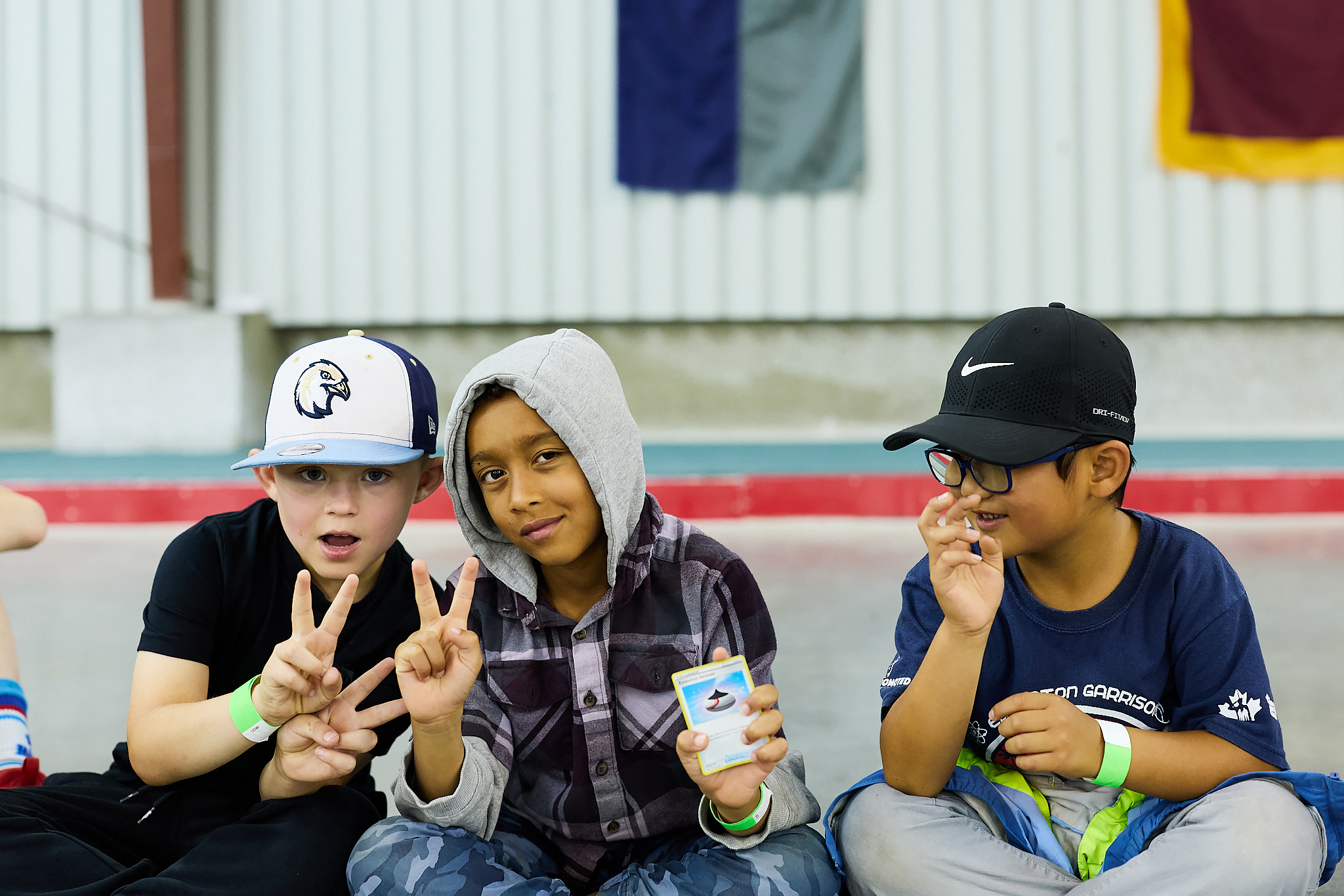 3 School aged children casually smiling at the camera holding a pokemon card