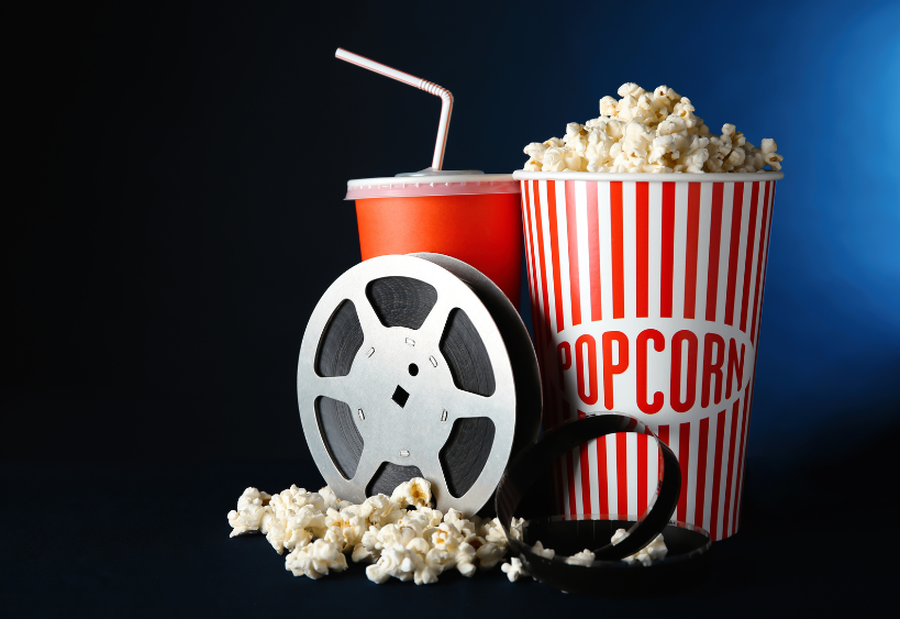 A picture of a film reel, popcorn and a fountain beverage