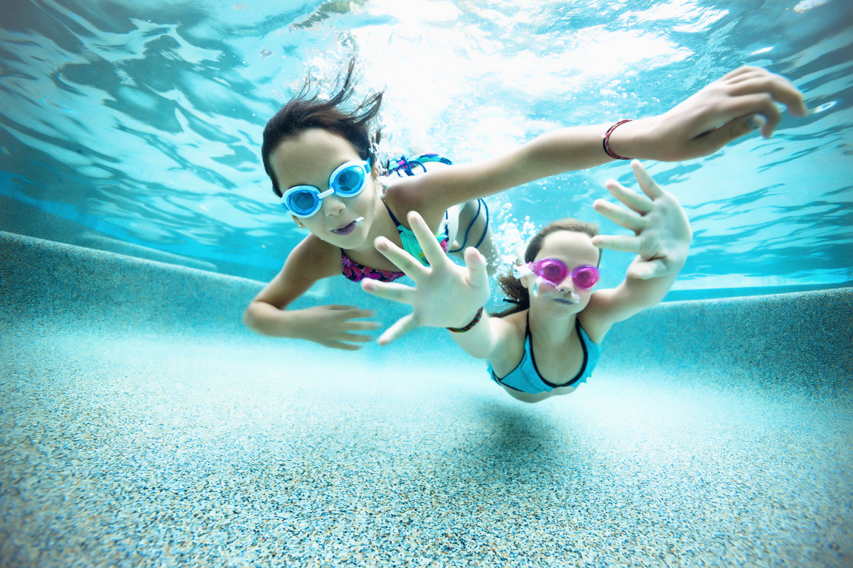 An underwater picture of 2 children wearing goggles swimming 
