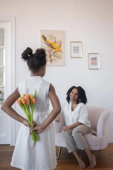 A daughter holding flowers behind her back, waiting to give to her Mom