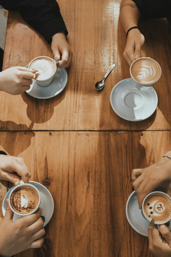 Four people holding their latte mugs at a table